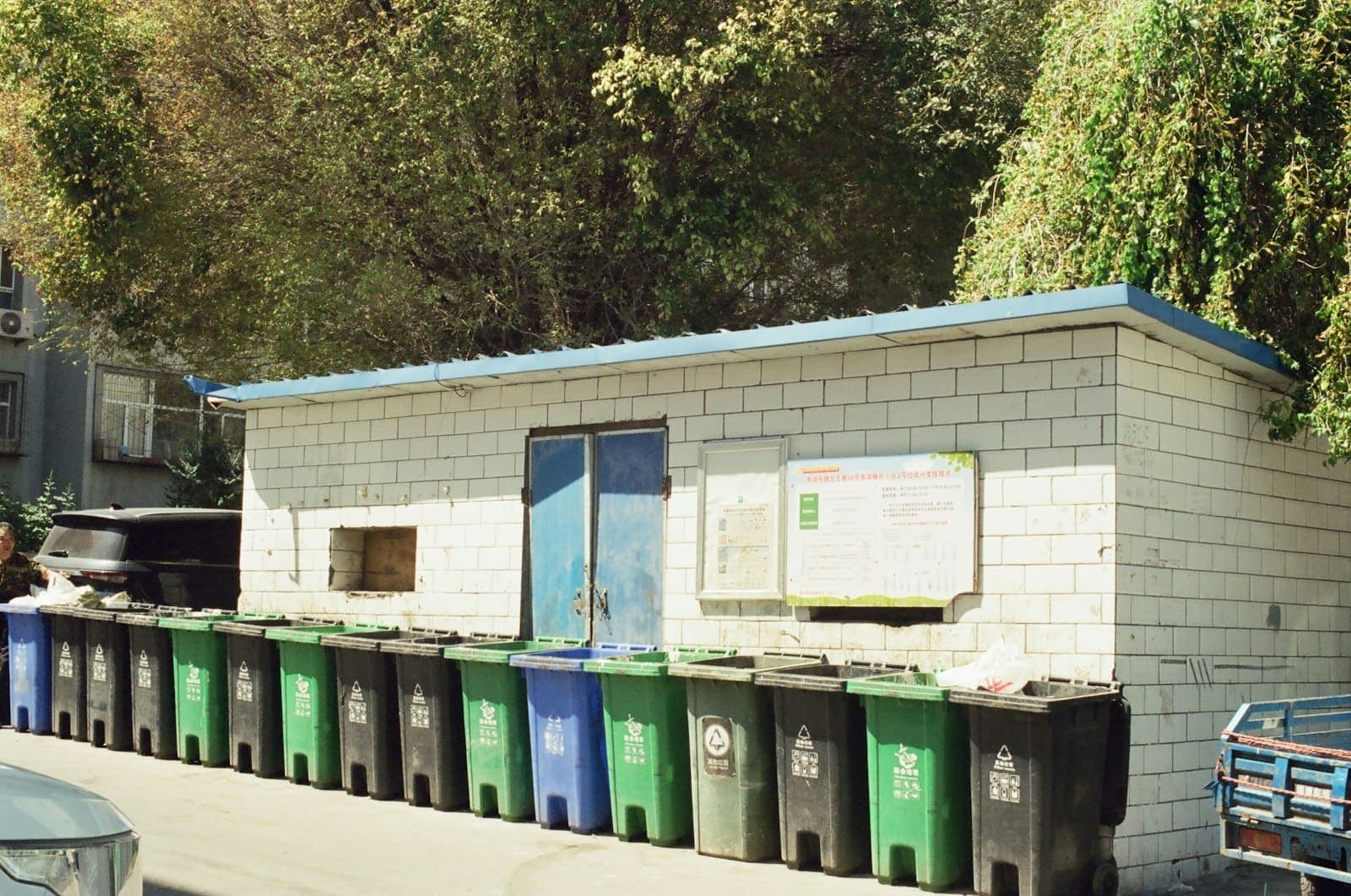 Fileira de lixeiras verdes e azuis ao lado de um prédio