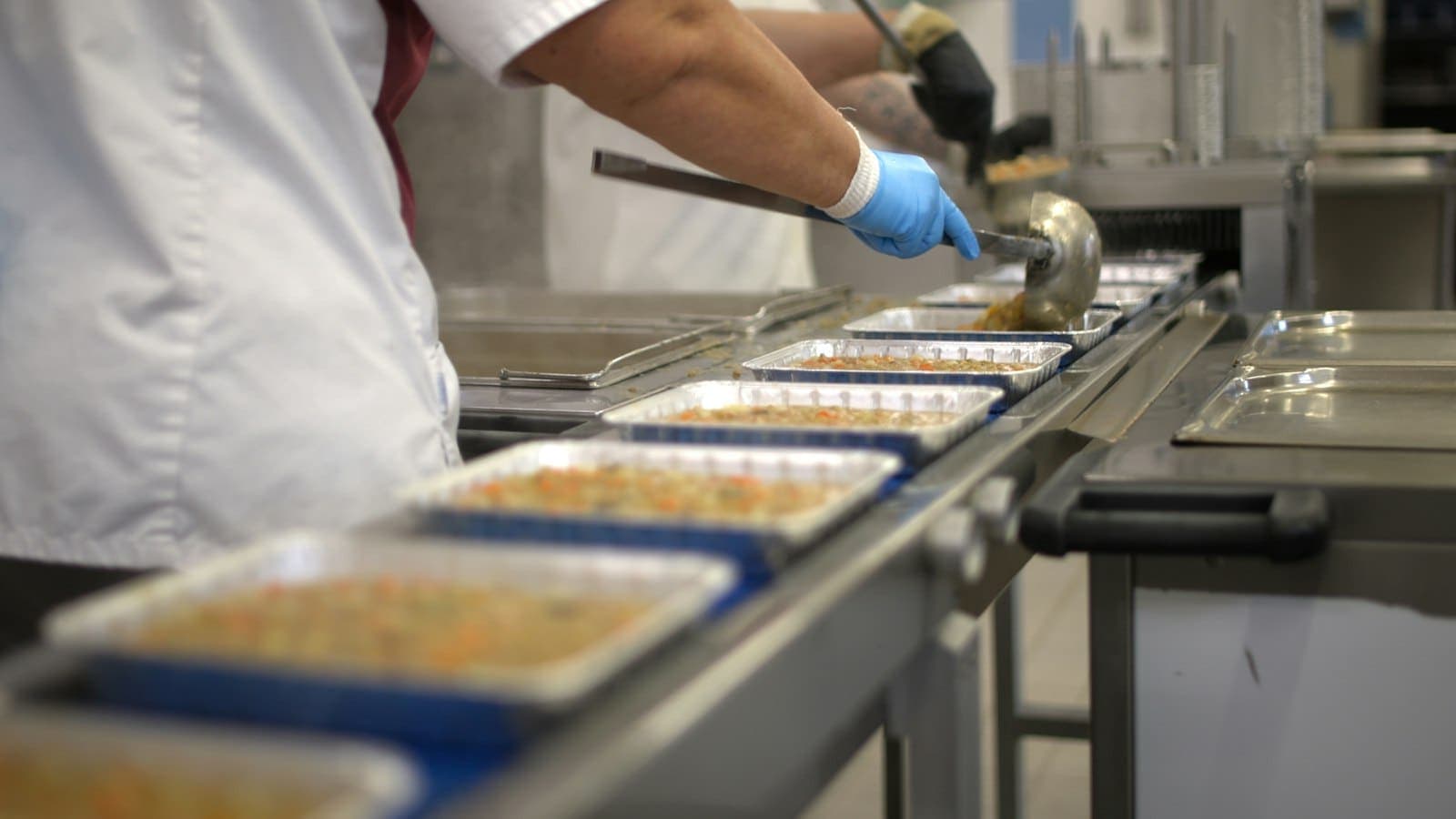 Funcionário de cozinha industrial enchendo marmitas em uma esteira