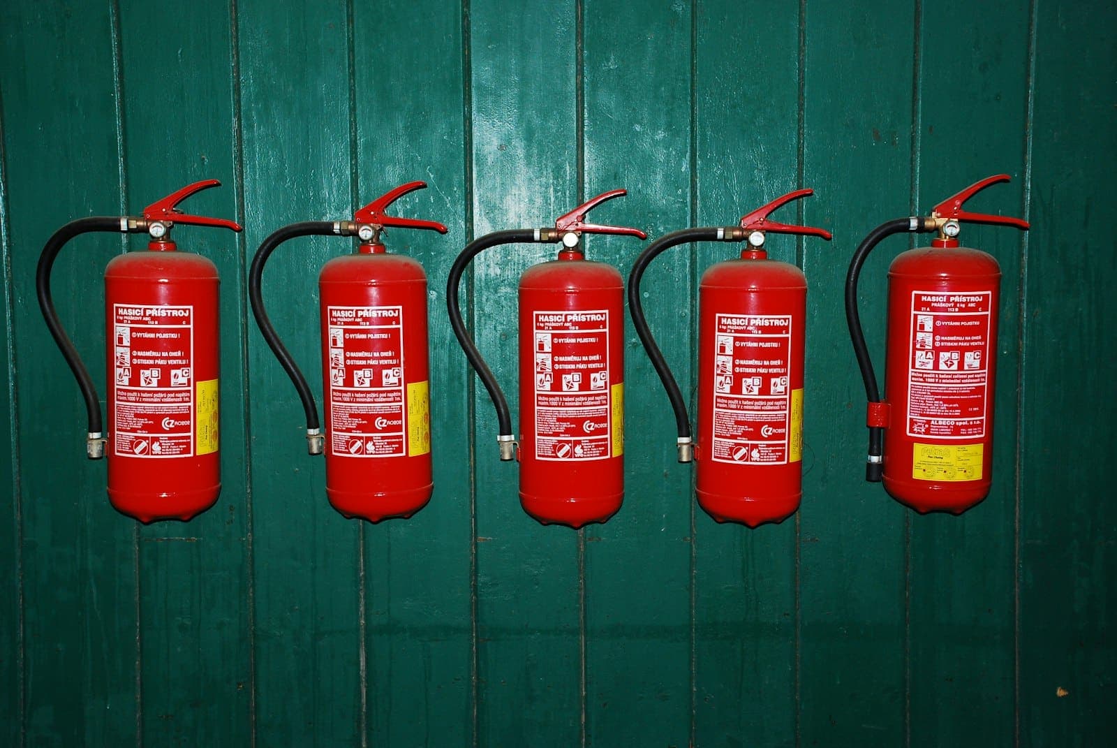 Extintores de incêndio vermelhos enfileirados em uma parede verde