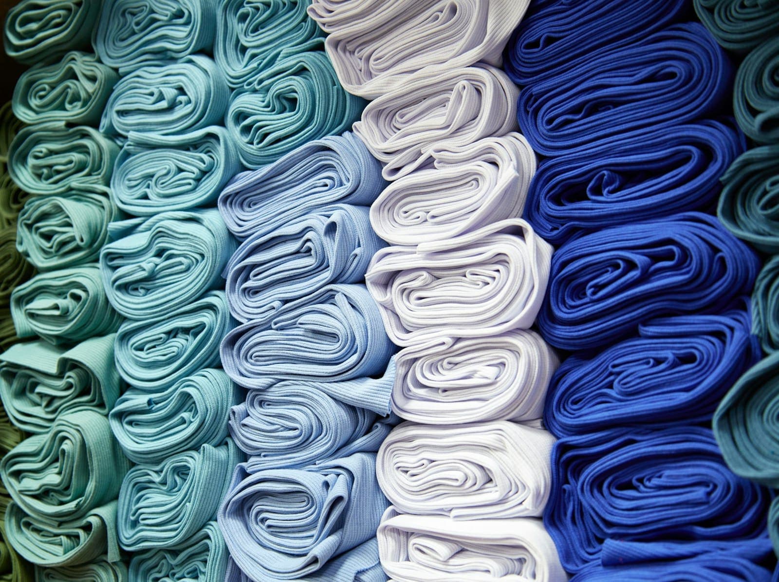 Tecidos dobrados e empilhados em tons de azul, verde e branco