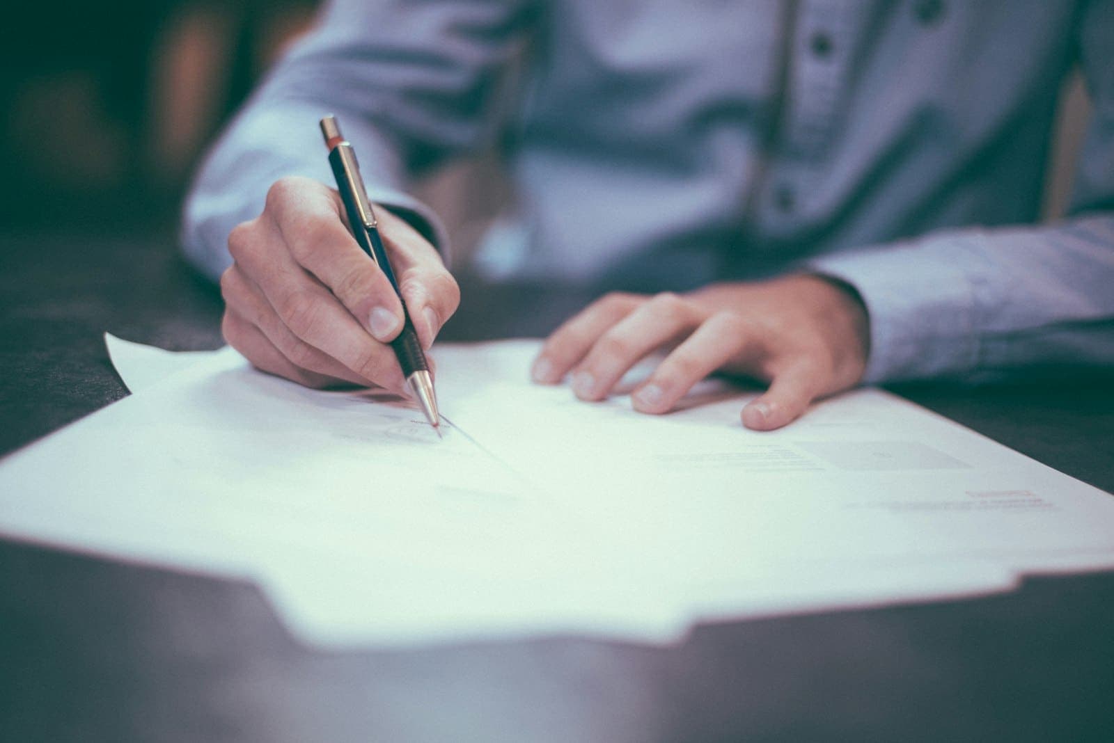 Mão com caneta preenchendo e assinando um documento em papel sobre a mesa