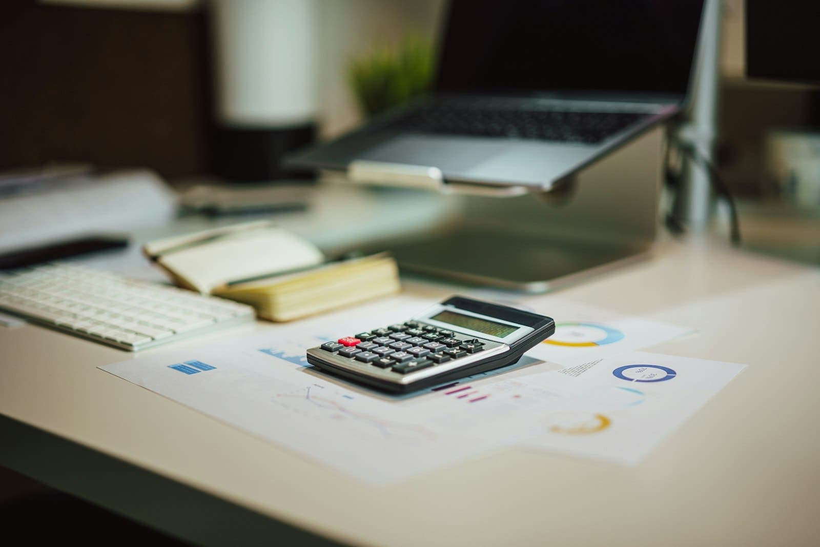 Calculadora sobre a mesa ao lado de um notebook e de relatórios com gráficos